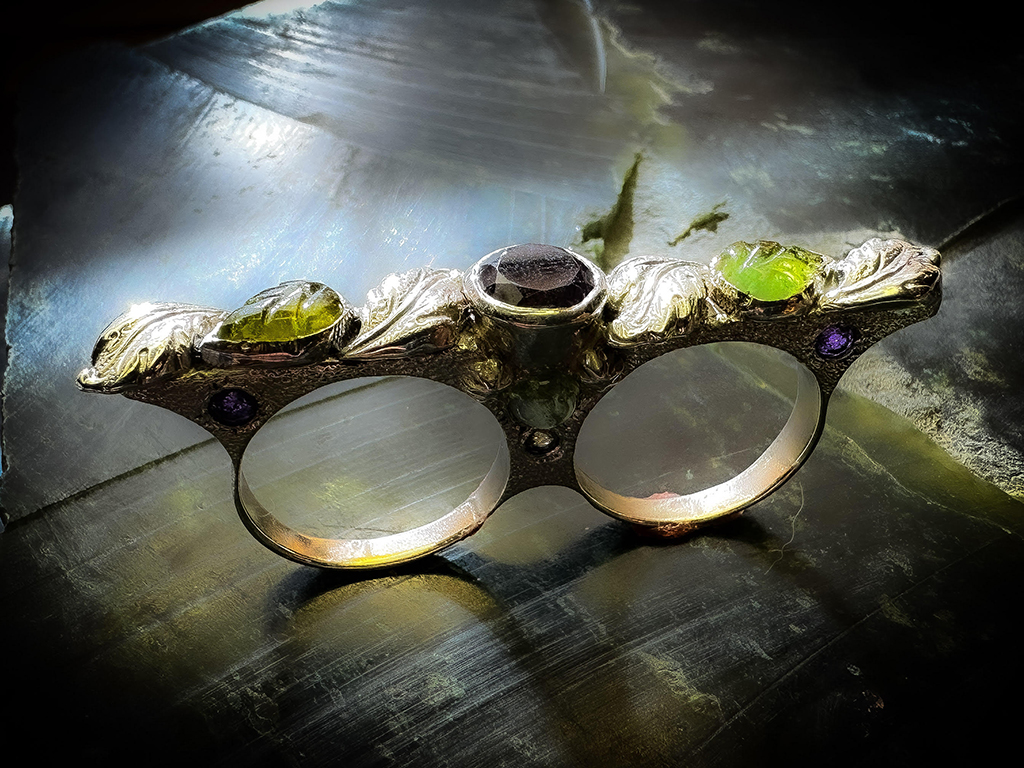 two finger hollow form ring in sterling silver, adorned with leaf shot made with Kevin Potter's plates. The ring itself has 11 set stones including amethyst, vintage tourmaline leaf carvings, citrine, and peridot.